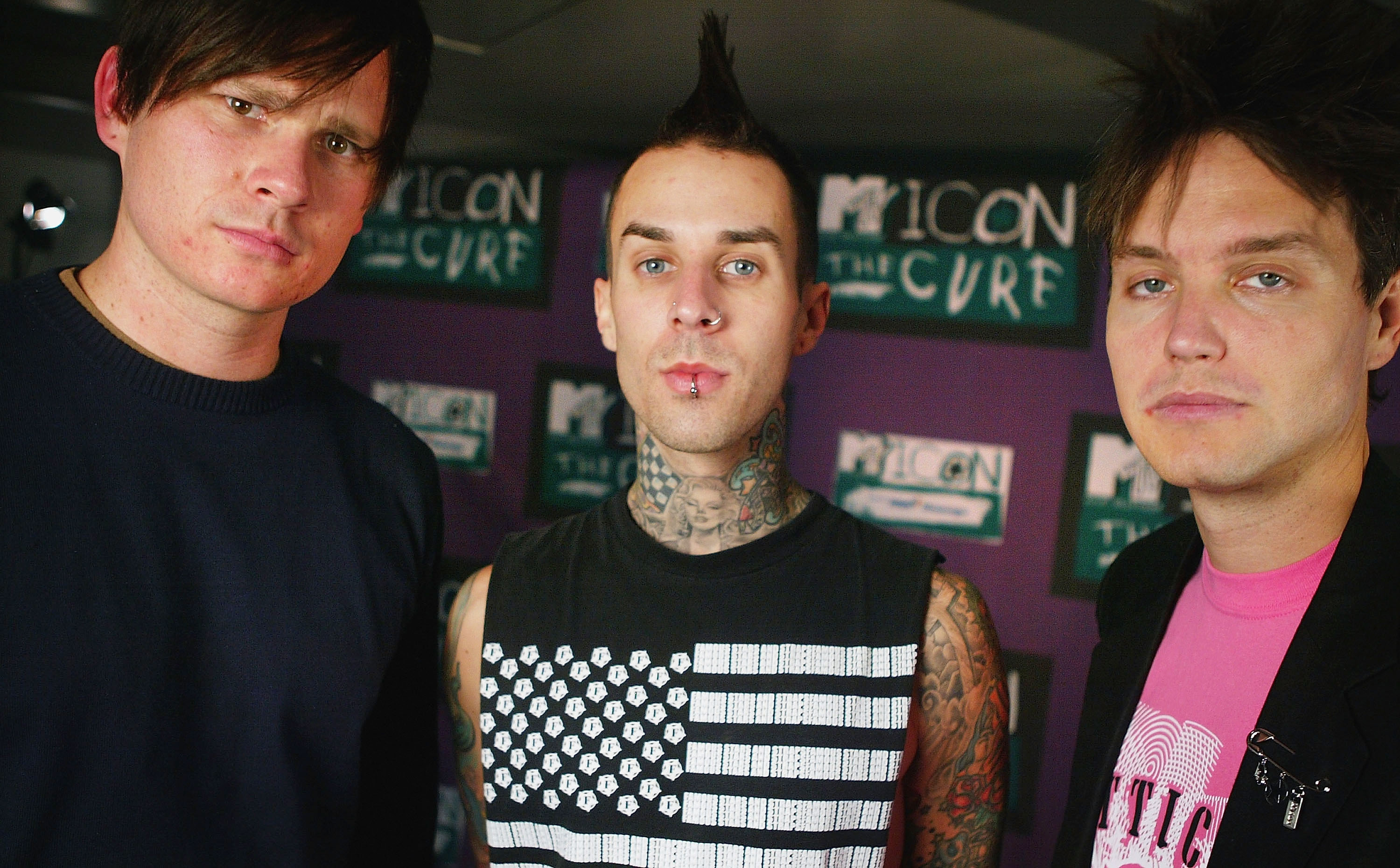 Three men standing together in front of MTV Icon The Cure branded backdrops; the middle man has a mohawk and neck tattoos.