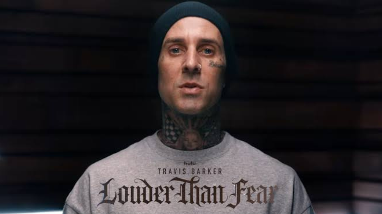 Man with neck tattoos and dark beanie wearing a grey sweatshirt reading 'Travis Barker: Louder Than Fear' on Hulu.