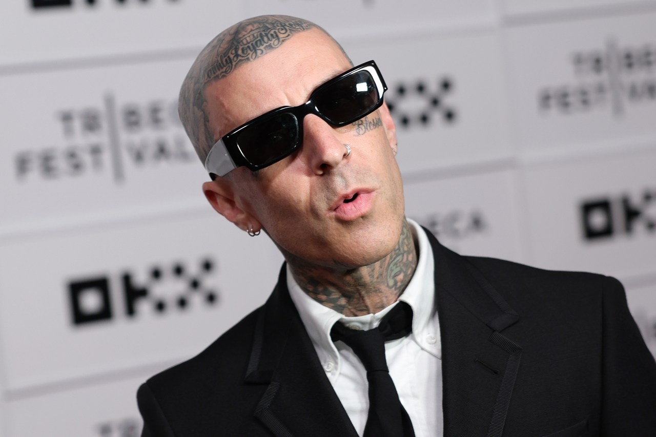 Close-up of a heavily tattooed man in a black suit and black rectangular sunglasses at a Tribeca Festival media wall.