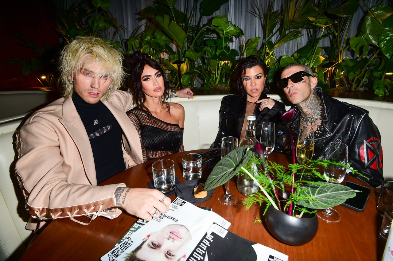 Four people — a man with wild blonde hair, a dark-haired woman in black mesh, another dark-haired woman, and a tattooed man in sunglasses — seated at a restaurant table.