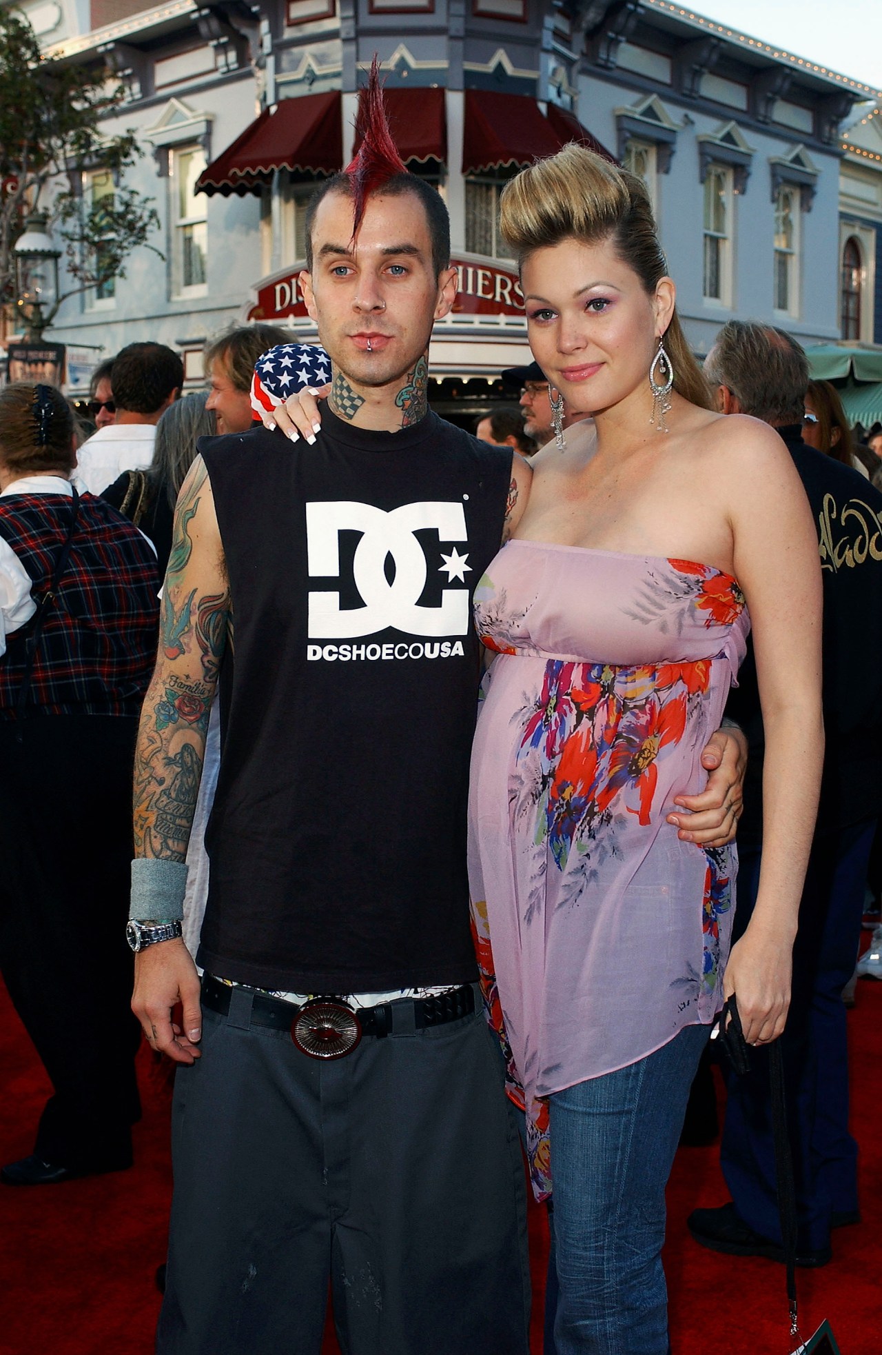 Man with red mohawk and tattooed arms in a DC Shoes tank top standing with a blonde woman in a floral strapless top on a red carpet at Disneyland.