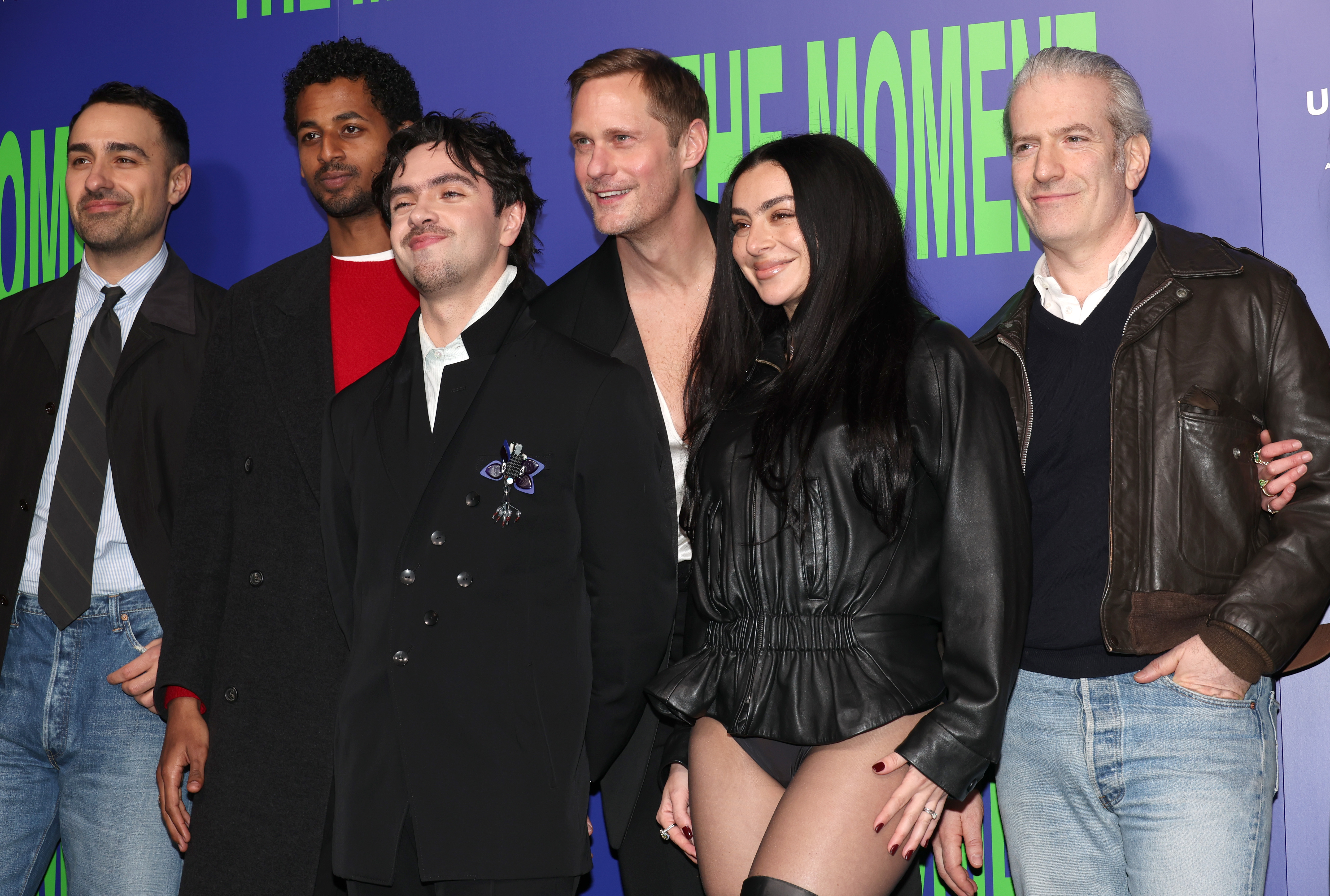 Six people posing together at The Moment UK premiere in front of a blue and green backdrop at Picturehouse Central, London.