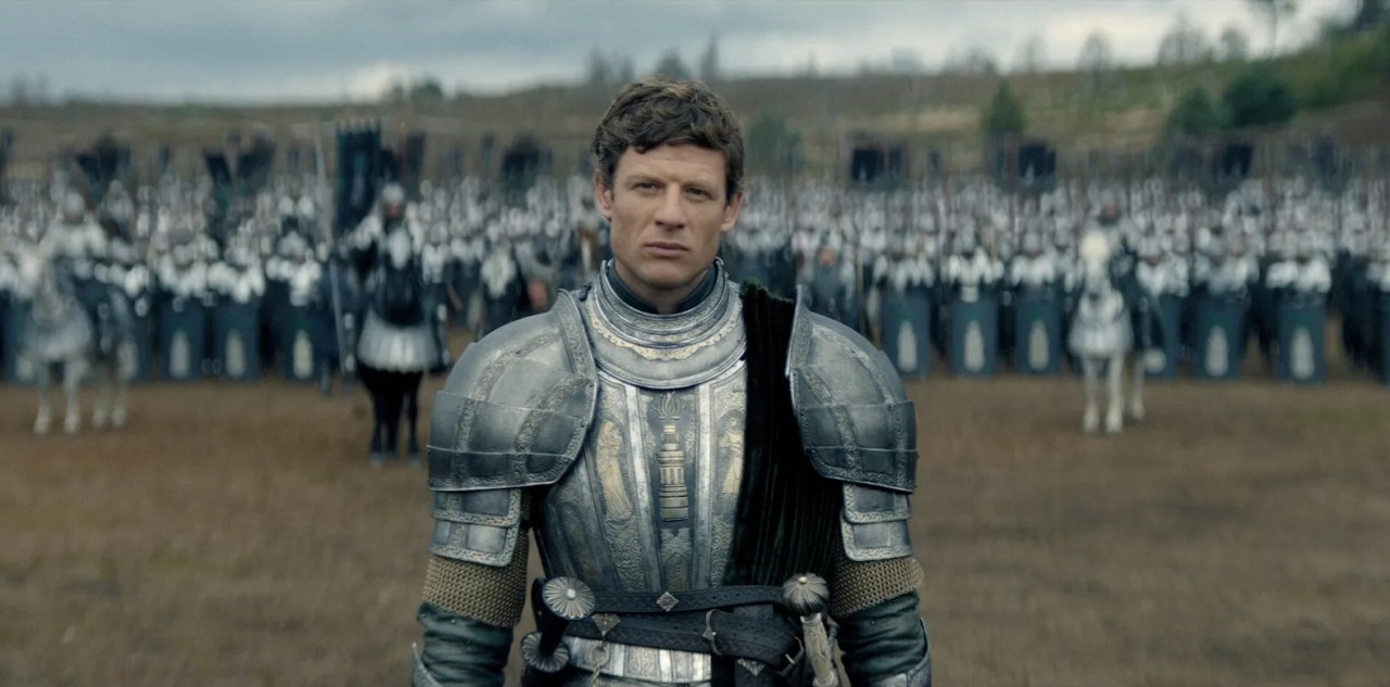 Man in elaborate engraved silver plate armor stands on a battlefield with rows of armored soldiers behind him.